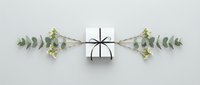 White gift box with black ribbon bow surrounded by eucalyptus branches on clean background for holiday celebrations and special occasions.