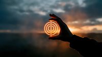 Hand holding glowing circular target symbol against dramatic sunset sky with storm clouds creating powerful business goal achievement concept.
