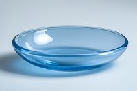 Empty blue glass bowl with transparent curved edges on white background, minimalist tableware design suitable for modern kitchen and dining decor.