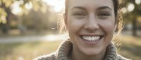 Young Caucasian woman with bright smile wearing cozy sweater outdoors in warm golden sunlight during autumn season for lifestyle and wellness concepts.