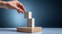 Female hand placing wooden cube block on stacked blocks against blue gradient background, representing business growth, strategy and development process.