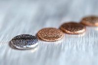 Metallic glitter coins in silver and rose gold colors arranged in diagonal line on white textured background, shallow depth of field creates dreamy effect.