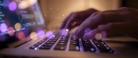 Hands typing on laptop keyboard with glowing digital particles and purple bokeh lights creating futuristic technology atmosphere for business presentations.