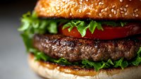 Juicy grilled beef burger patty with fresh lettuce, tomato slices and sesame bun in macro shot, dark background with selective focus on meat.