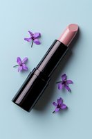 Pink lipstick in black tube with scattered purple spring flowers on light blue background, minimal cosmetic flatlay composition for beauty and makeup advertising.