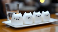 Adorable white cat-shaped desserts with cute faces arranged on plate in cozy cafe setting for kawaii food photography and culinary art concepts.
