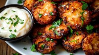 Crispy pan-seared potato medallions garnished with fresh herbs and served with creamy dipping sauce on rustic white plate, close up view of appetizer.