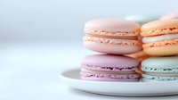 Pastel colored French macarons in pink, peach, lavender and mint arranged on white plate against light background, selective focus on delicate meringue cookies.