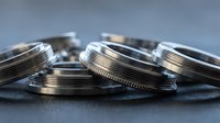 Stack of silver metal lens filters with ribbed edges arranged on dark textured surface for photography equipment and camera accessories.