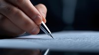 Close-up of hand holding pen signing document on dark background, business contract or legal agreement concept for corporate professionals.