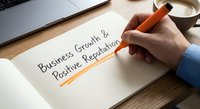 Business professional writing growth and positive reputation strategy on paper with orange highlighter at modern office desk workspace.