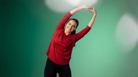 Young Hispanic woman in red top doing side stretch exercise against green blurred background. Fitness wellness lifestyle concept for health and workout routines.