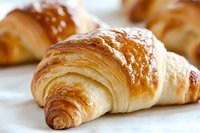 Fresh baked golden croissant with flaky layered texture and crispy crust on white background, close up view showing buttery pastry details.