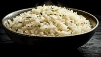 Steamed white basmati rice garnished with fresh herbs in rustic black bowl on dark wooden background, dramatic side lighting creates appetizing texture.