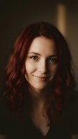 Young Caucasian woman with auburn wavy hair smiling warmly in soft natural lighting. Portrait photography with shallow depth of field for lifestyle content.