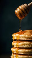Golden honey dripping from wooden dipper onto stack of fluffy pancakes against dark background for breakfast and cooking concepts.