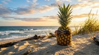 Fresh pineapple on sandy beach at golden sunset with ocean waves and driftwood creating tropical paradise vacation mood for summer travel concepts.
