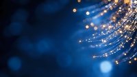 Glowing optical fibers with golden sparkles and light trails against deep blue background create magical atmosphere for technology and communication concepts.
