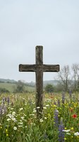 Weathered wooden cross stands in vibrant wildflower meadow with daisies and lupines under overcast sky for memorial or spiritual concepts.
