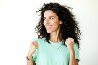 Happy young woman with curly hair celebrating success with raised fists in mint green shirt on white background for motivational content.