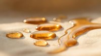 Golden amber liquid droplets and viscous flows on neutral surface, suitable for health supplements, skincare products, cosmetics, and wellness marketing materials.