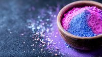 Vibrant pink and blue powder pigments in wooden bowl on dark background with scattered particles, dramatic lighting creates mystical atmosphere.