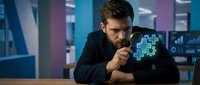 Focused Caucasian businessman examining glowing digital gear puzzle with magnifying glass in modern office, concept of problem solving.