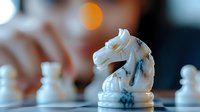 White chess knight piece in sharp focus with blurred hand and chess pieces in background, strategic board game concept for business and planning.