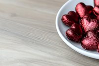 Red foil wrapped chocolate hearts in white bowl on wooden table for Valentine's Day celebration and romantic occasions.