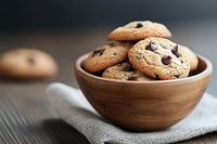 Freshly baked chocolate chip cookies in wooden bowl on linen napkin. Homemade sweet treats for bakery, cafe menu, dessert recipes and comfort food concepts.