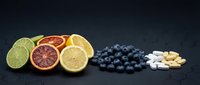 Fresh citrus fruits, blueberries and vitamin supplements arranged on dark slate background for healthy lifestyle and nutrition concepts.