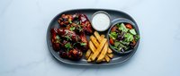 Grilled chicken wings with herbs served on dark plate alongside fresh salad, golden fries and creamy dipping sauce for restaurant menu photography.