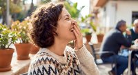 Young woman with curly hair laughing joyfully outdoors in cozy sweater. Candid moment of happiness and positive emotions in casual lifestyle setting.