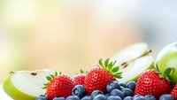 Fresh mixed berries and apple slices arranged on white surface with soft natural lighting background for healthy eating and nutrition concepts.