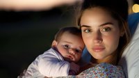 Young mother holding sleeping baby at night, intimate moment captured in soft warm light against dark background, expressing maternal love and tenderness.