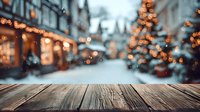 Rustic wooden table with blurred Christmas market street view in background, decorated with festive lights and snow-covered stalls.