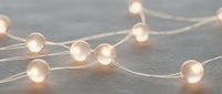 Warm glowing string lights with soft spherical bulbs draped across neutral surface, creating ambient lighting for home decor, events, and festive celebrations.
