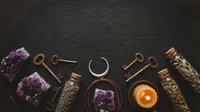 Mystical collection of amethyst crystals, vintage keys, candle and spiritual tools arranged on dark slate background for meditation and healing practices.