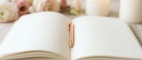 Open notebook with blank pages and gold pen, surrounded by soft flowers and candles, perfect for journaling, writing, planning, and creative projects.