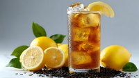 Refreshing iced tea with lemon slices and fresh lemons on gray background, garnished with green leaves and tea leaves.