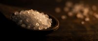 Coarse sea salt crystals in wooden spoon on rustic table for cooking and seasoning culinary preparations.