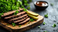Juicy sliced beef steak on wooden cutting board garnished with fresh parsley and lime wedges, served with sauce. Dark moody food photography.