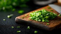 Fresh chopped green onions on rustic wooden cutting board against dark background, macro food photography with selective focus and natural light.