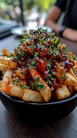 Gourmet loaded fries topped with caramelized onions, fresh herbs and sesame seeds served in black bowl at restaurant for food photography and menu design.