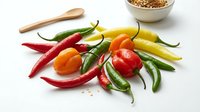 Fresh colorful hot chili peppers variety including red, green, yellow and orange peppers with wooden spoon and spices bowl on white background.