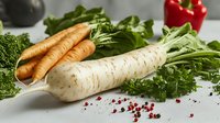 Fresh daikon radish and carrots with green leaves on light background, scattered pink peppercorns. Raw organic vegetables for healthy cooking.