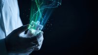 Hands holding glowing holographic digital interface with green and blue light particles on dark background, representing technology innovation and future communication.