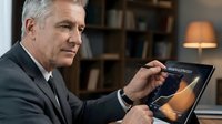 Mature Caucasian businessman in suit using digital tablet for online banking and financial management in modern office environment.