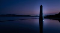 Wooden post standing in calm water at twilight with purple and blue sky reflecting on still lake surface, serene landscape.