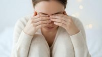 Young Caucasian woman covering eyes with hands wearing cream sweater against soft bokeh background expressing surprise anticipation or playful emotion.